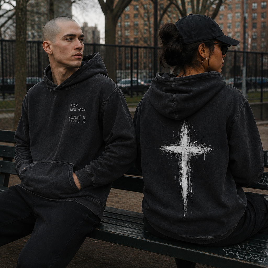 Two people sitting on a bench wearing FØR Cross hoodies, one showing the front text and the other showing the back with a cross design.