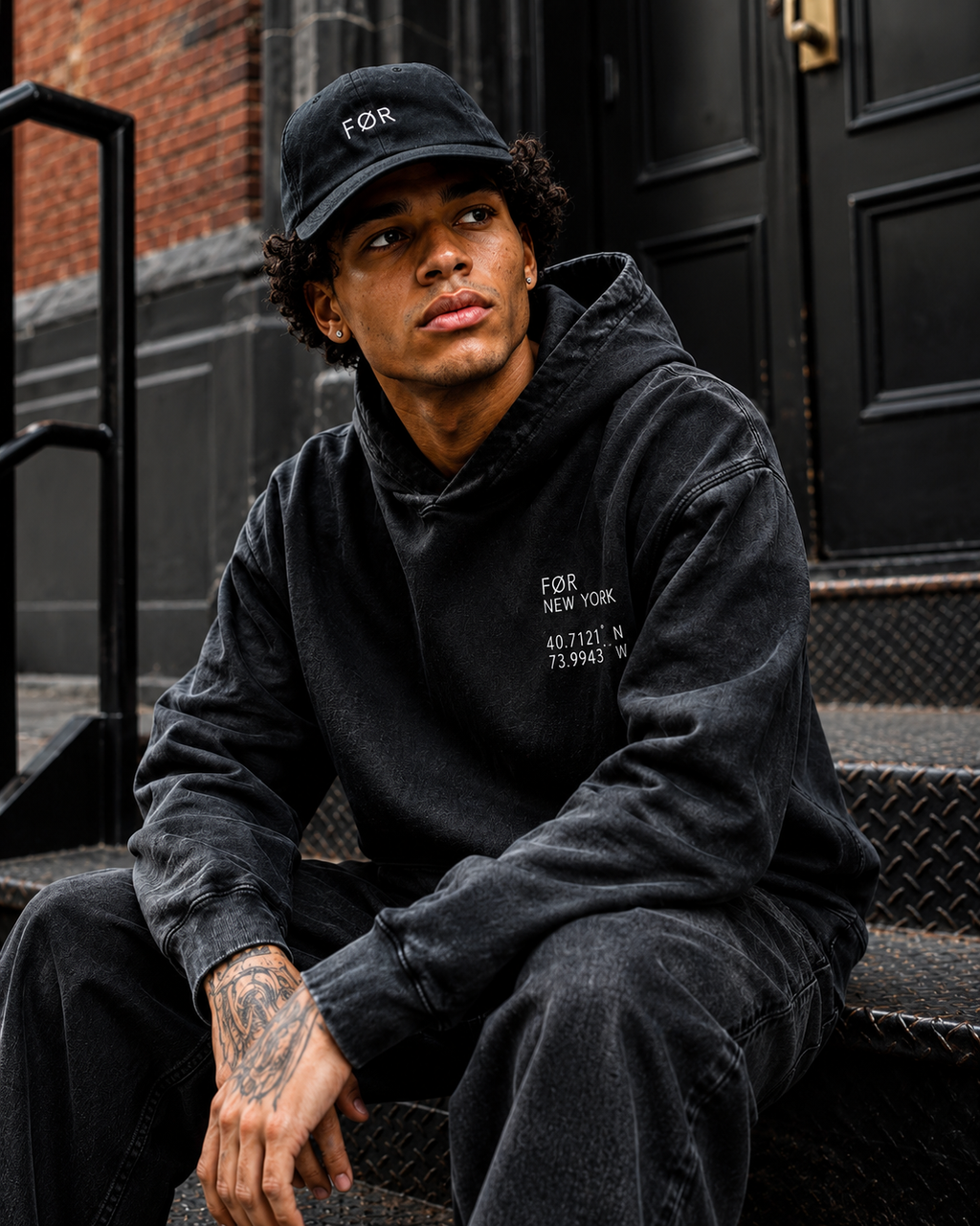 Person wearing a FØR black hoodie and cap sitting on steps.